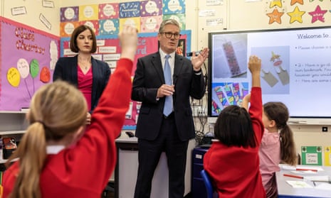 Keir Starmer takes questions from children in a year three class: he faces the children and three small girls in red jumpers are seen from behind with their hands up.