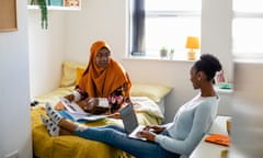 Two female uni student friends sitting in their dorm bedroom are studying together while sitting on the bed in the North East of England. They are using laptops/have their work files in front of them.