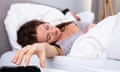 Young Woman Sleeping On Bed Turning Off Alarm Clock In Bedroom