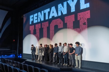 A line of more than 10 teenagers stand on stage in spotlights with screen that says Fentanyl High behind them.