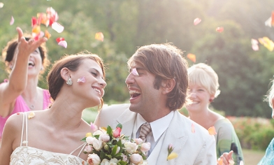 A couple getting married, smiling at each other, with confetti thrown at them from guests left and right