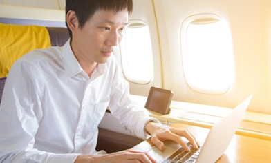 Man on plane in upgraded seating working on his laptop