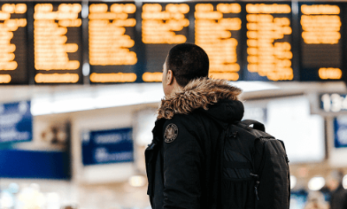 Male wearing winter jacket and backpack looking up at departures board