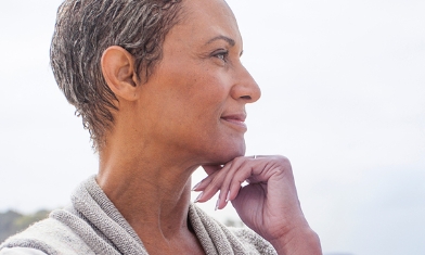 Lady beneath an overcast sky, hand under chin, looking in to the distance