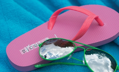 A pair of green sunglasses laid on top of a pink flip flop on top of a blue blanket