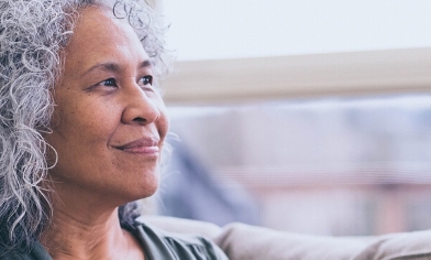 Mature woman sat on a couch, smiling as she looks out of the nearby window