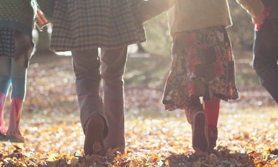 Family in winter clothing walking amongst fallen autumn leaves under the sun