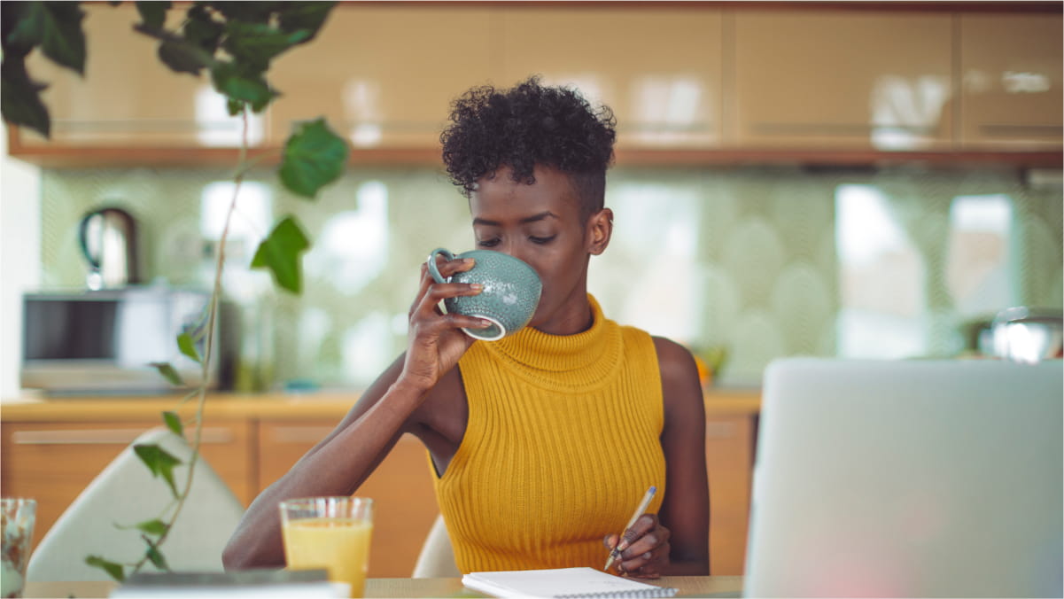 Female sitting at the desk, drinking from a mug and holding a pen in the other hand