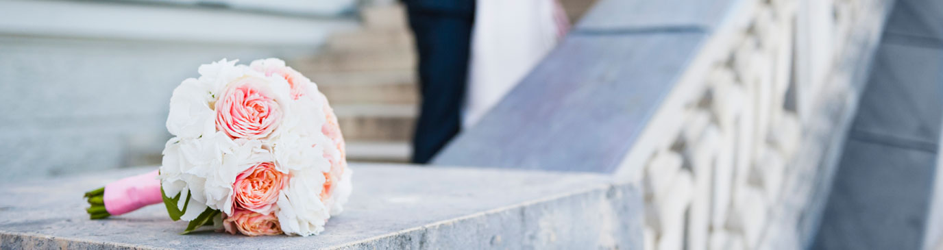 Wedding bouquet with pink and white roses, sat on stone stair bannister, bride & groom in distance