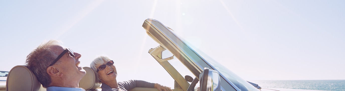 A senior couple driving a convertible on a sunny day, smiling, wearing sunglasses