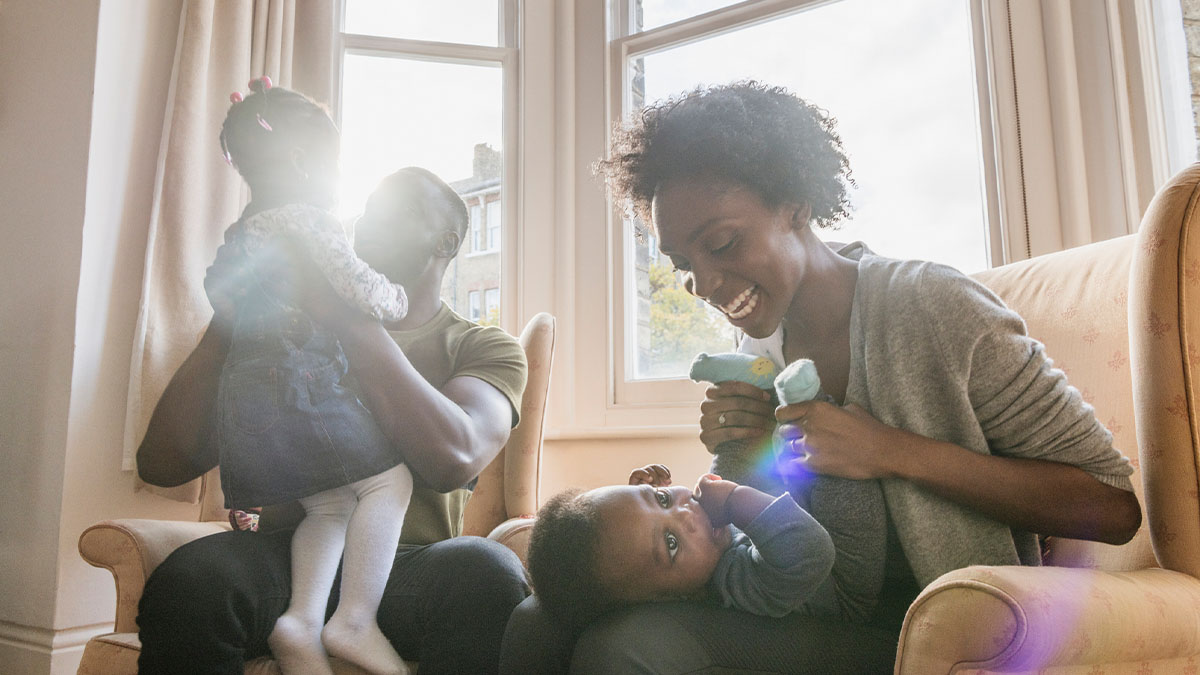 Smiling mother and father sat on their living room sofa playing with their young daughters