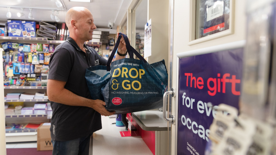 Male customer holding a drop and go bag ready to hand over a counter at a Post Office branch