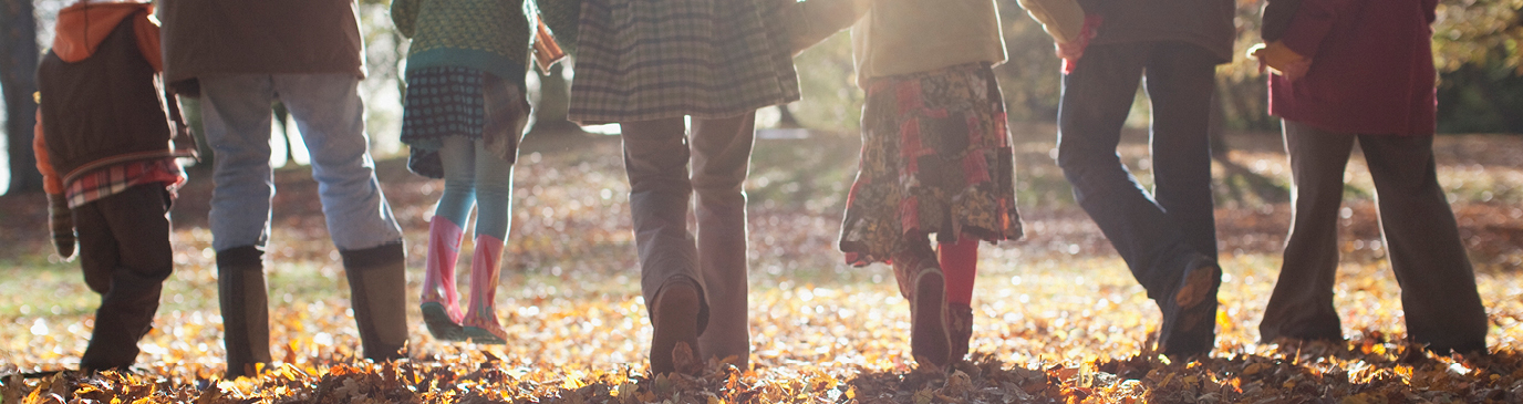 Family in winter clothing walking amongst fallen autumn leaves under the sun