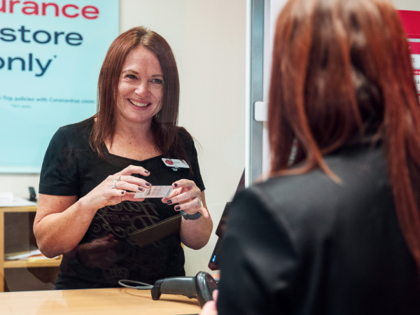 A female member of Post Office staff at a counter in branch looking at the ID of her customer