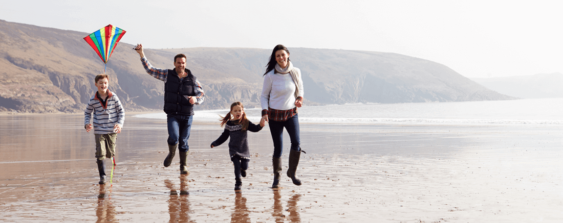 Family walking on a beach flying a kite